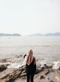 Rear view of woman standing on beach against clear sky