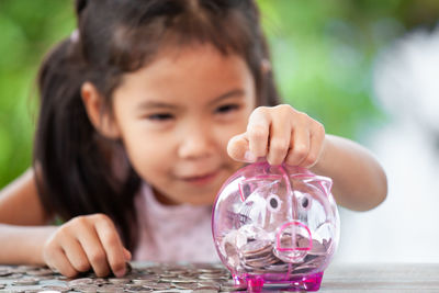 Girl putting coin in piggy bank at table