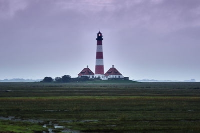 Lighthouse on field by building against sky