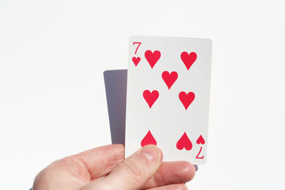 Close-up of hand holding seven of hearts playing card over white background