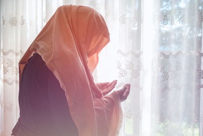 Side view of woman standing by window at home