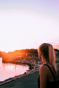 Side view of woman looking at sea against sky during sunset