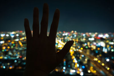 Hand holding illuminated cityscape against sky at night