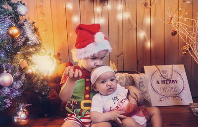 Siblings sitting by christmas decorations at home