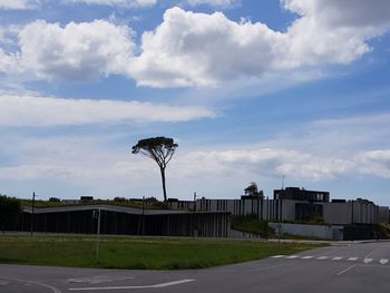 Road by building against cloudy sky