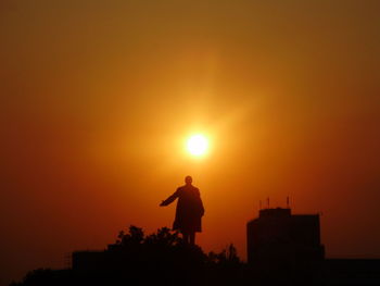 Silhouette man standing against orange sky during sunset