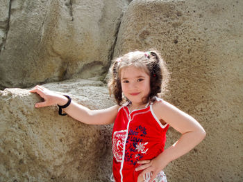 Portrait of smiling girl with hand on hip standing by rock formation