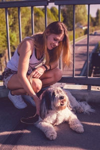 Smiling young woman crouching by dog on footbridge