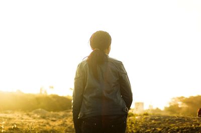 Rear view of mid adult woman standing on field against clear sky