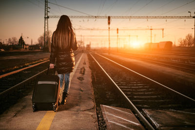 Rear view of woman on railroad tracks against sky during sunset