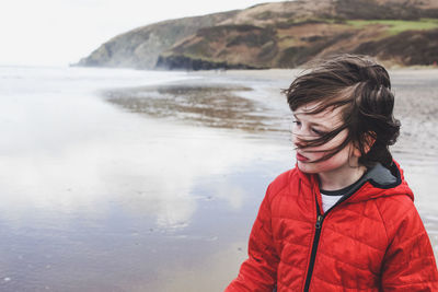 Boy with tousled hair looking at view while standing on shore