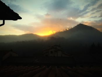 Silhouette houses and mountains against sky during sunset