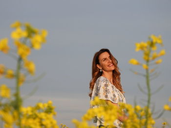 Young woman standing on yellow flower against sky