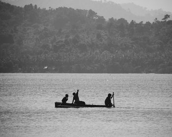 Silhouette people sitting in boat on lake against trees