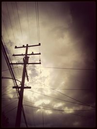 Low angle view of electricity pylon against cloudy sky