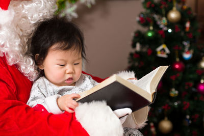 Close-up of santa claus and baby girl reading book at home