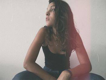 Low angle view of young woman sitting against white wall at home