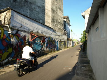 Rear view of man riding motorcycle on street by graffiti wall