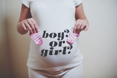 Midsection of pregnant woman holding baby booties against wall