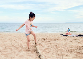Pretty young girl is trying to walk and balance on a tree branch on the beach