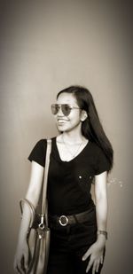 Portrait of young woman wearing sunglasses standing against wall