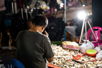 Rear view of man vendor at market during night