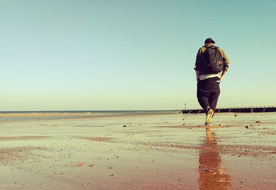 Rear view of man walking on beach against clear sky