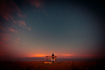 Rear view of man standing on field against sky at night