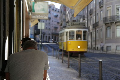 Rear view of man by tramway on sidewalk in city