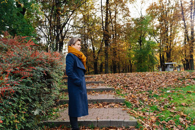 Side portrait of a short-haired blonde in a coat and scarf in autumn