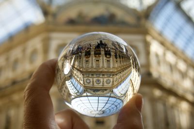 Cropped hand holding crystal ball against historical buildings 