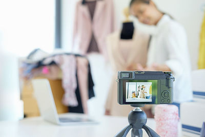 Camera photographing fashion designer with dress in office