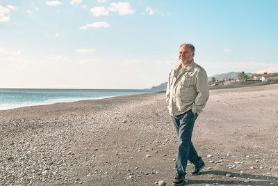 Happy middle-aged bearded man walking along deserted winter beach.