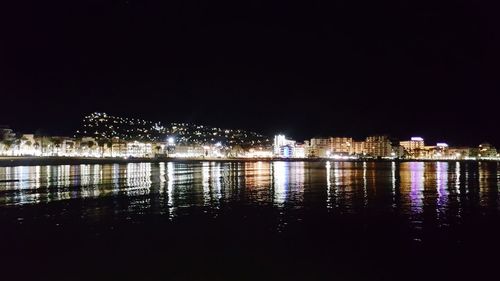 Illuminated buildings by lake against clear sky at night