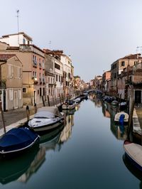 Boats moored in canal amidst buildings against clear sky