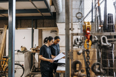Female employees discussing while doing paperwork in manufacturing warehouse