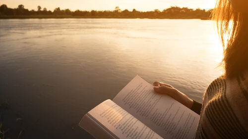 Young woman reading the book at riverside in the evening.