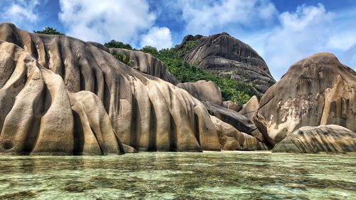 Rock formation in water against cloudy sky