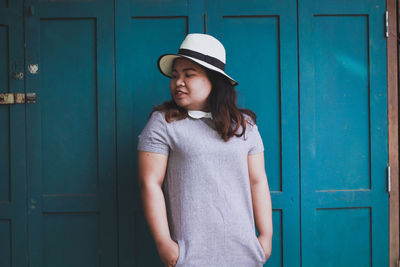 Young woman standing against blue door