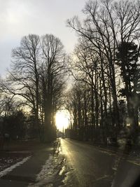 Road amidst bare trees against sky during sunset