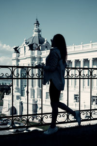 Rear view of woman walking on railing against buildings in city