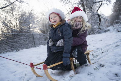 Happy brother and sister sitting on sled in snow