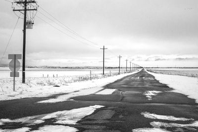 Road by electricity pylon against sky during winter