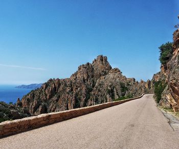 Road amidst trees against clear blue sky