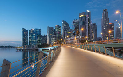Illuminated city at waterfront against blue sky