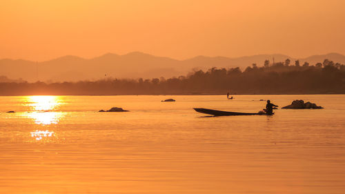 Silhouette man sailing boat in river against orange sky during sunset