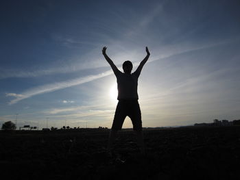 Silhouette man standing with arms raised on field against sky