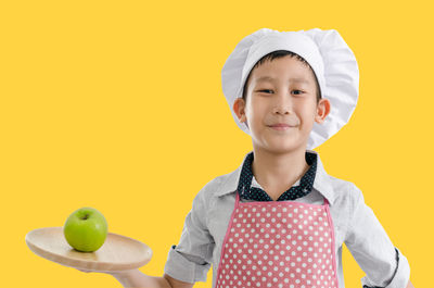 Portrait of cute boy holding apple against yellow background
