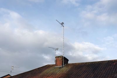 Low angle view of telephone pole on roof of building against sky