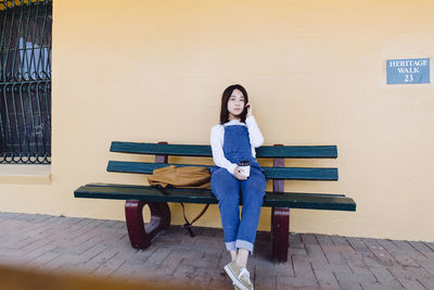 Portrait of woman sitting on bench against wall